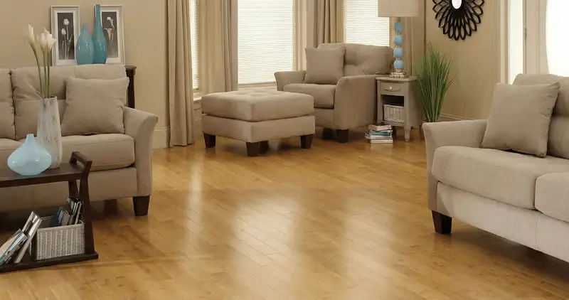 A living room with professionally installed bamboo flooring, beige sofas, a matching ottoman, a side table with a blue lamp, vases, framed pictures, and large windows with blinds and curtains in Minneapolis, MN
