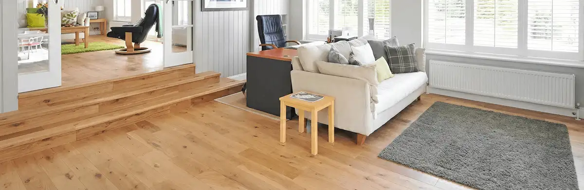 A modern living room with professionally installed laminate flooring, a beige sofa, a small side table, a gray rug, and large windows with white shutters in Minneapolis, MN
